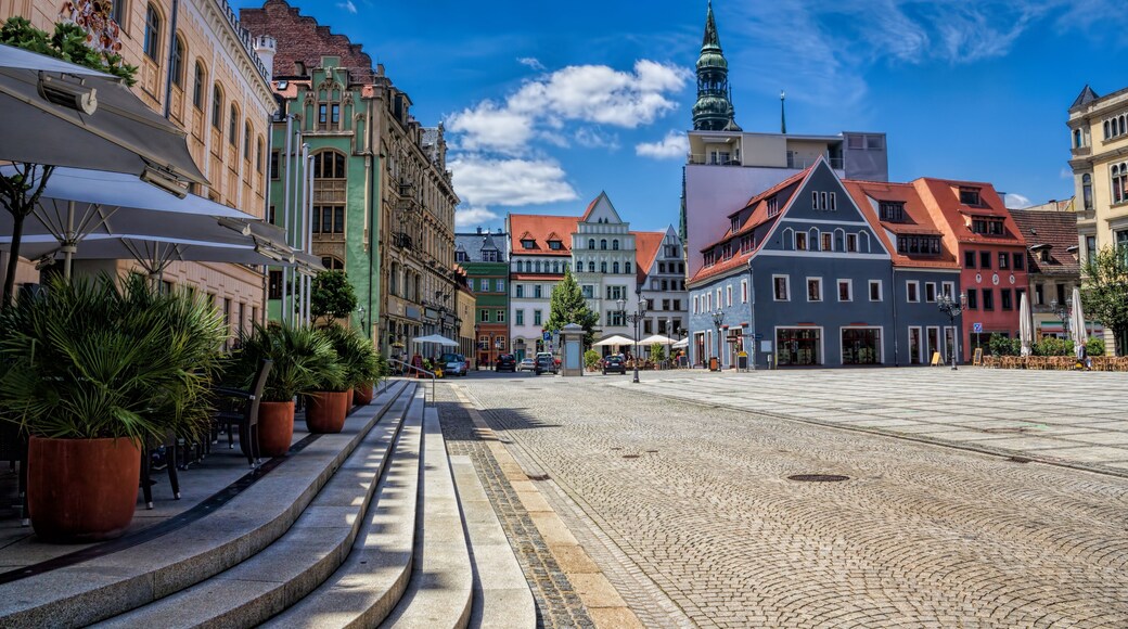 A cobblestone street lined with historic buildings, a church spire, and outdoor seating areas.