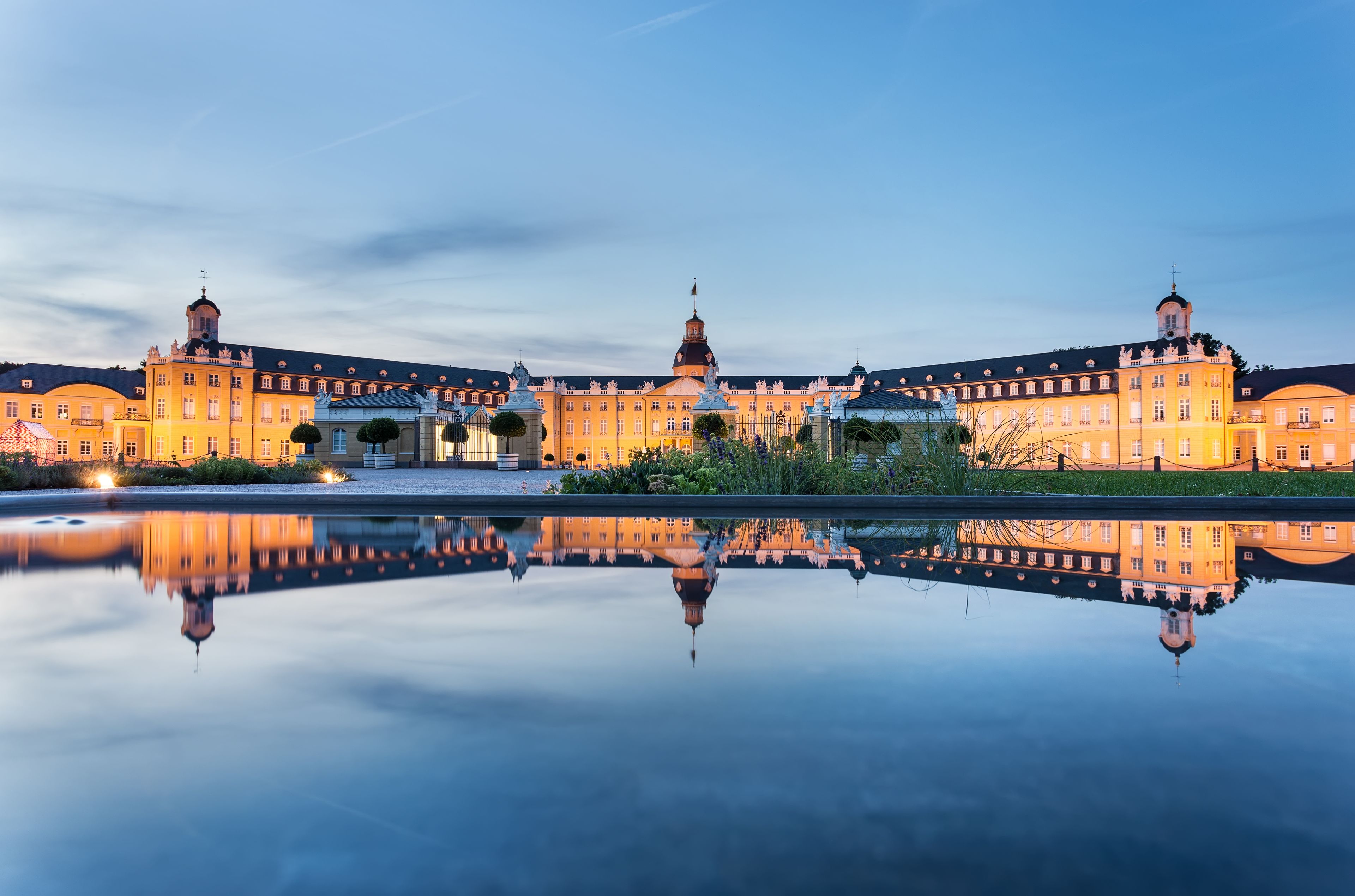 Un magnifique palais à la façade symétrique, doté d’une cour centrale et d’une surface d’eau qui reflète la lumière.