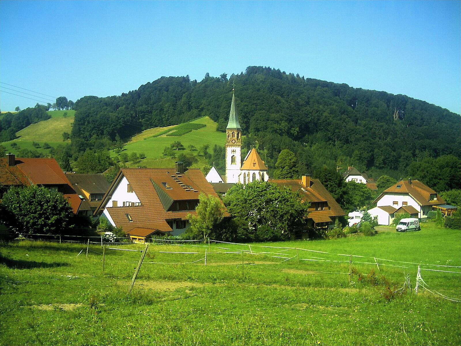 A village with a church, houses, and a green hill in the background.