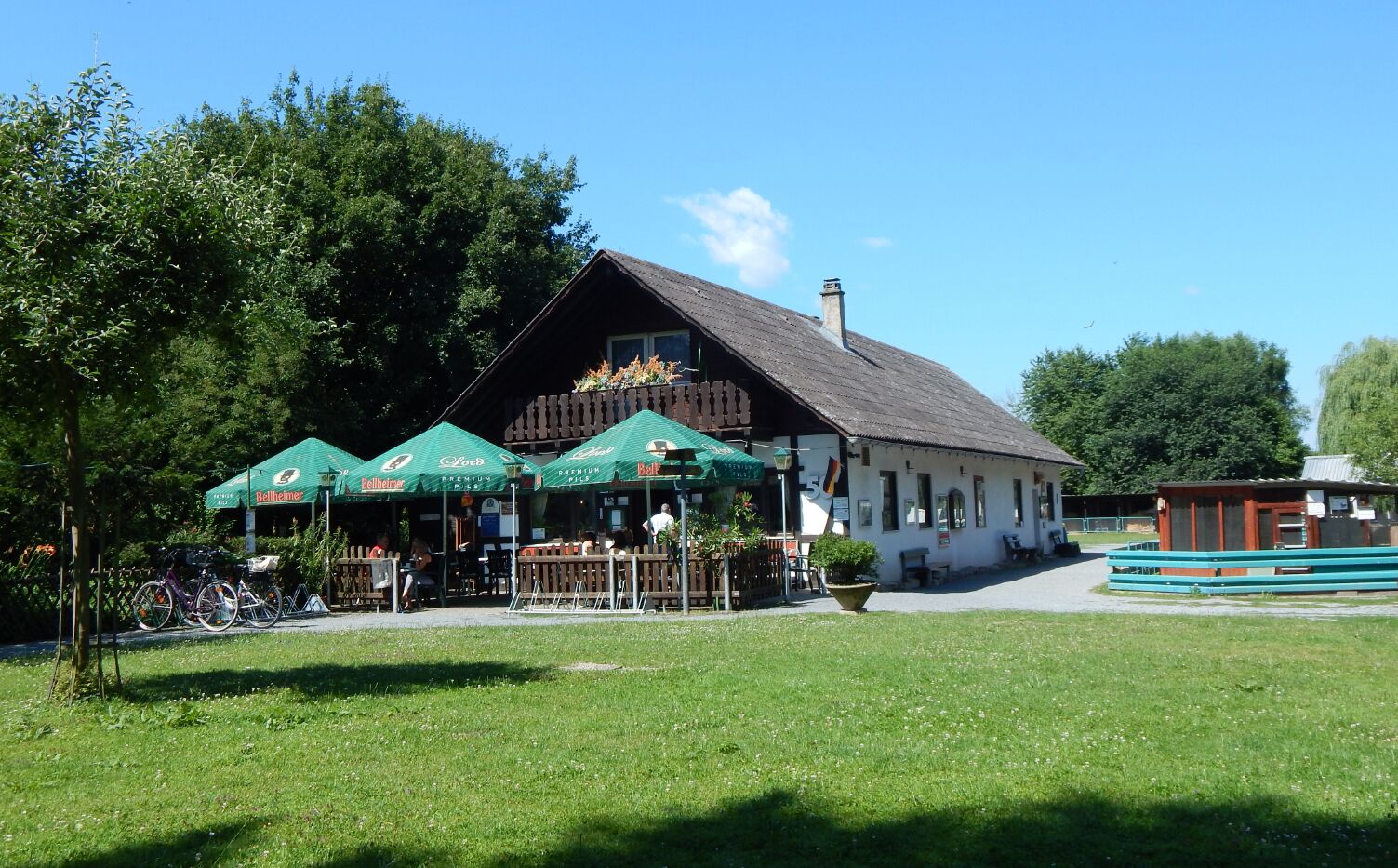A traditional wooden building with green umbrellas labeled "Bellheimer" in front.