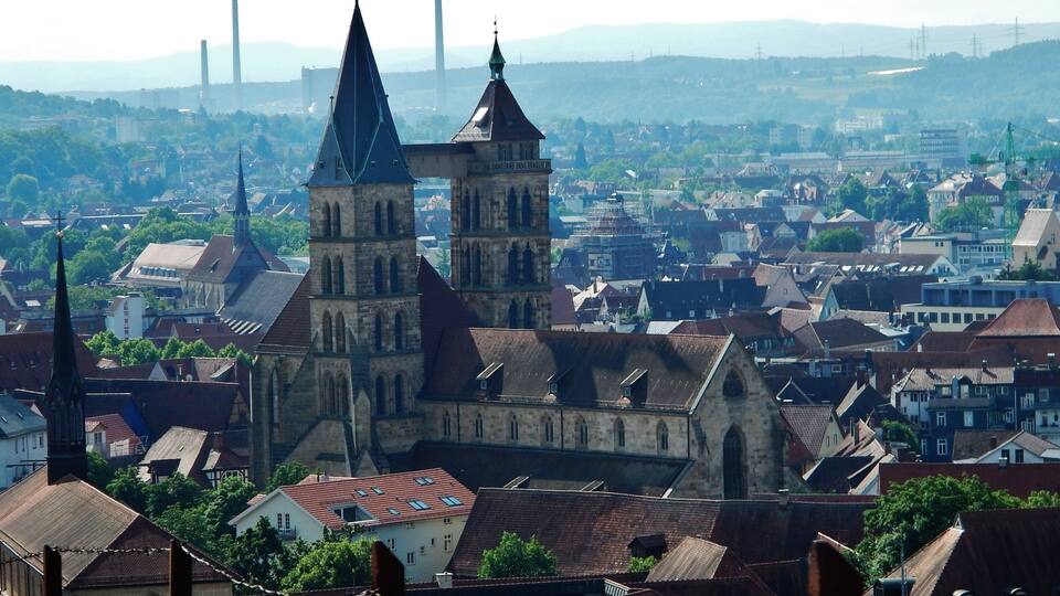 A historic church with two towers, surrounded by a cityscape with buildings and distant power lines.