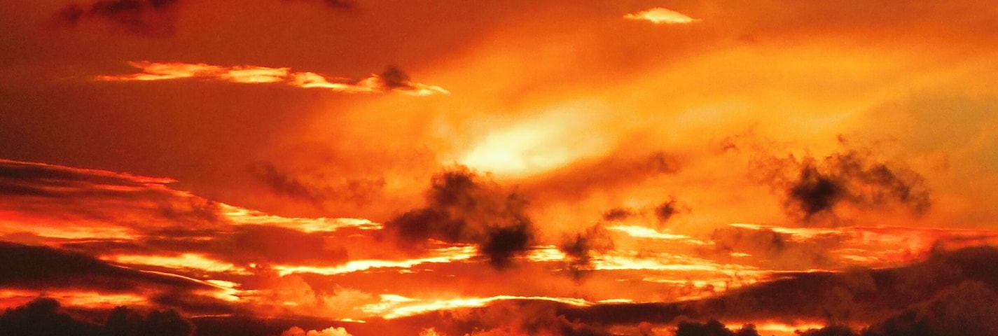 Un atardecer con la silueta de la aguja de una iglesia contra un cielo rojo intenso.