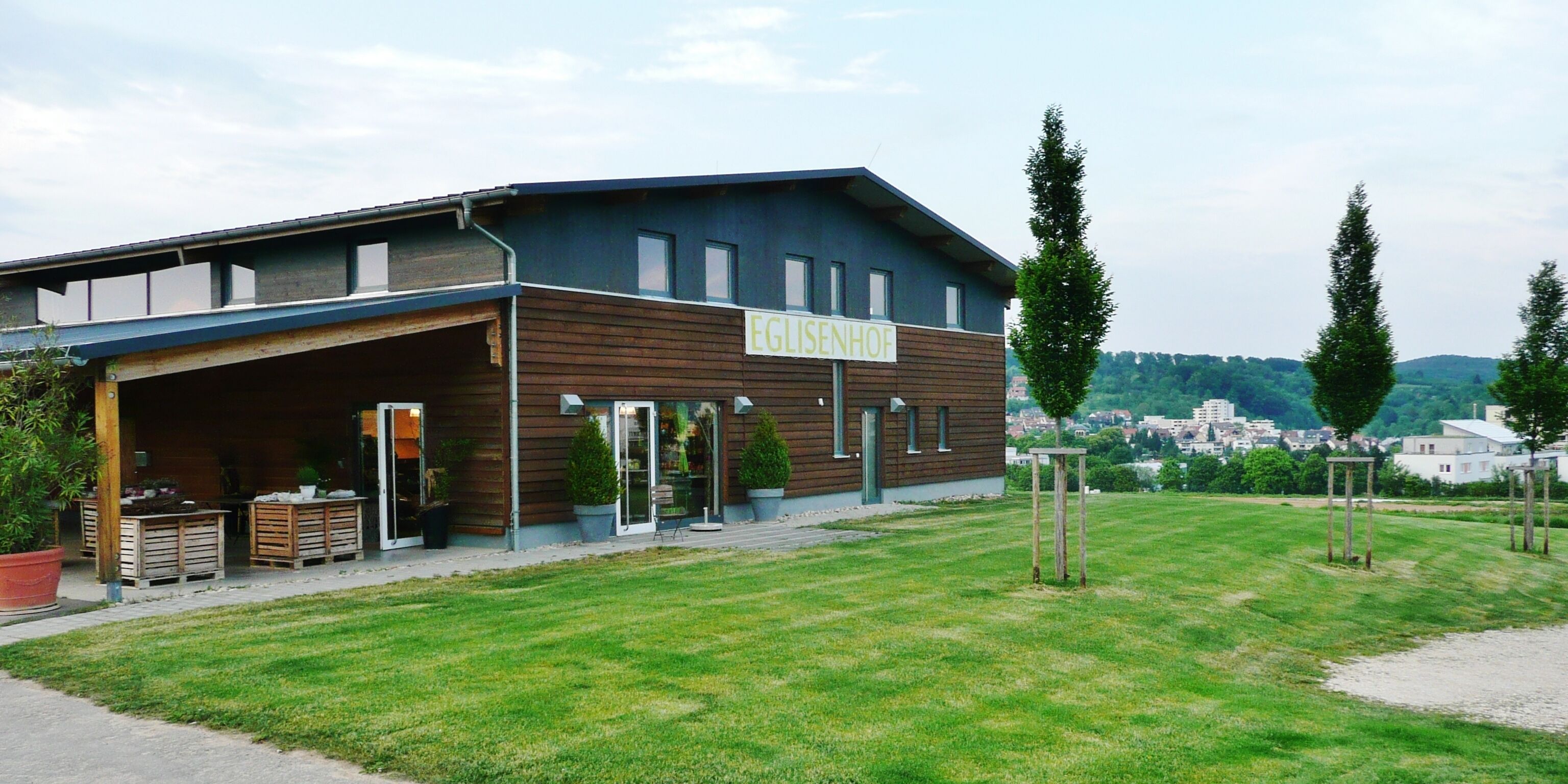 A building with a sign reading "EGELISENHOF" in a grassy area with trees and a distant view of a town.