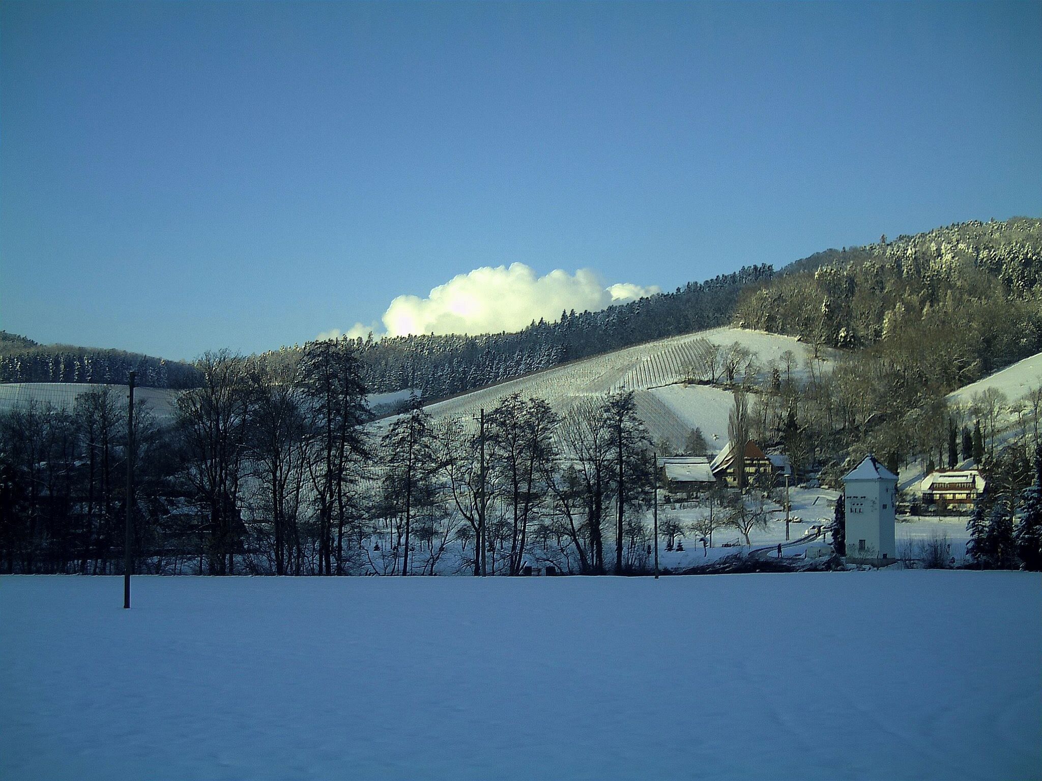 A snow-covered landscape with a village, a church, and a tower.