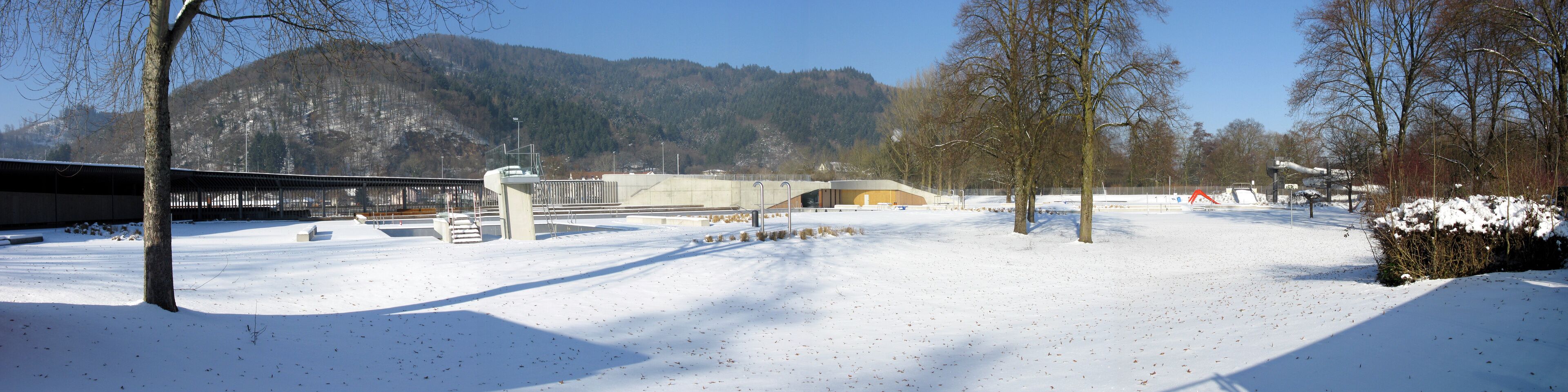 A snow-covered landscape with a bridge, buildings, and a mountain in the background.