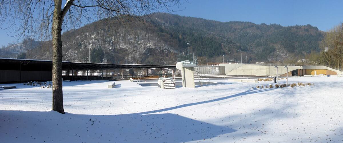 A snow-covered landscape with a bridge, buildings, and a mountain in the background.