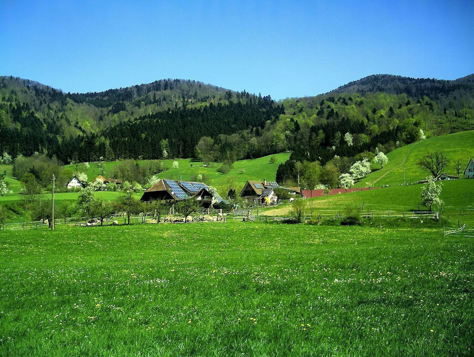 A rural landscape with rolling hills, a small village with traditional houses, and a clear blue sky.