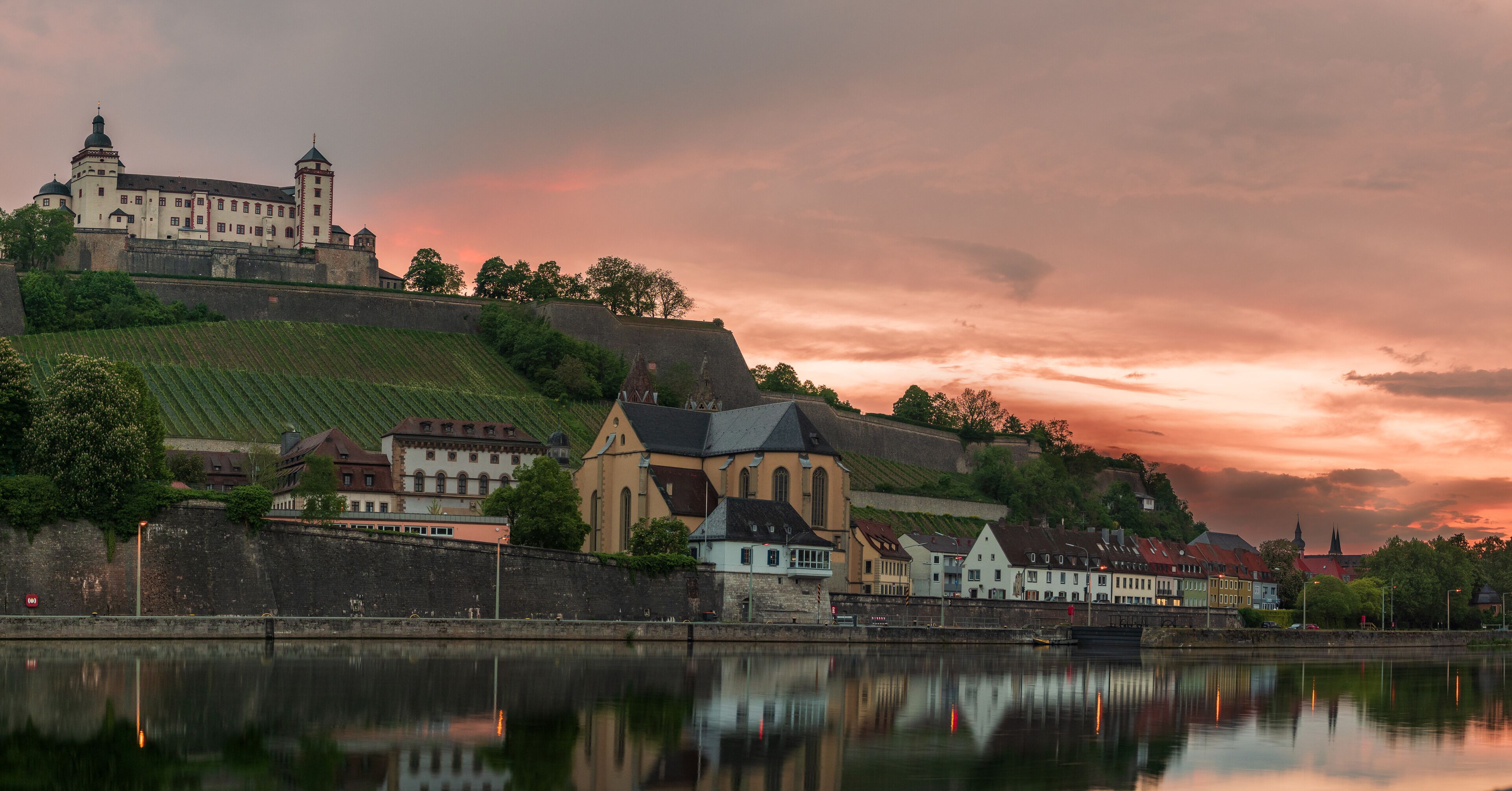 A historic town with a castle on a hill, a church, and a river reflecting the buildings.