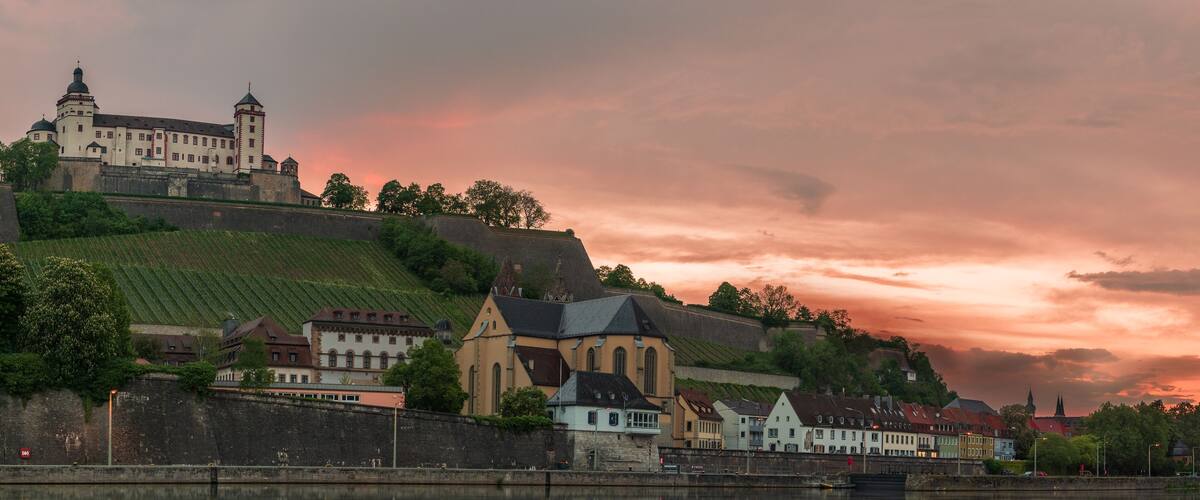 A historic town with a castle on a hill, a church, and a river reflecting the buildings.