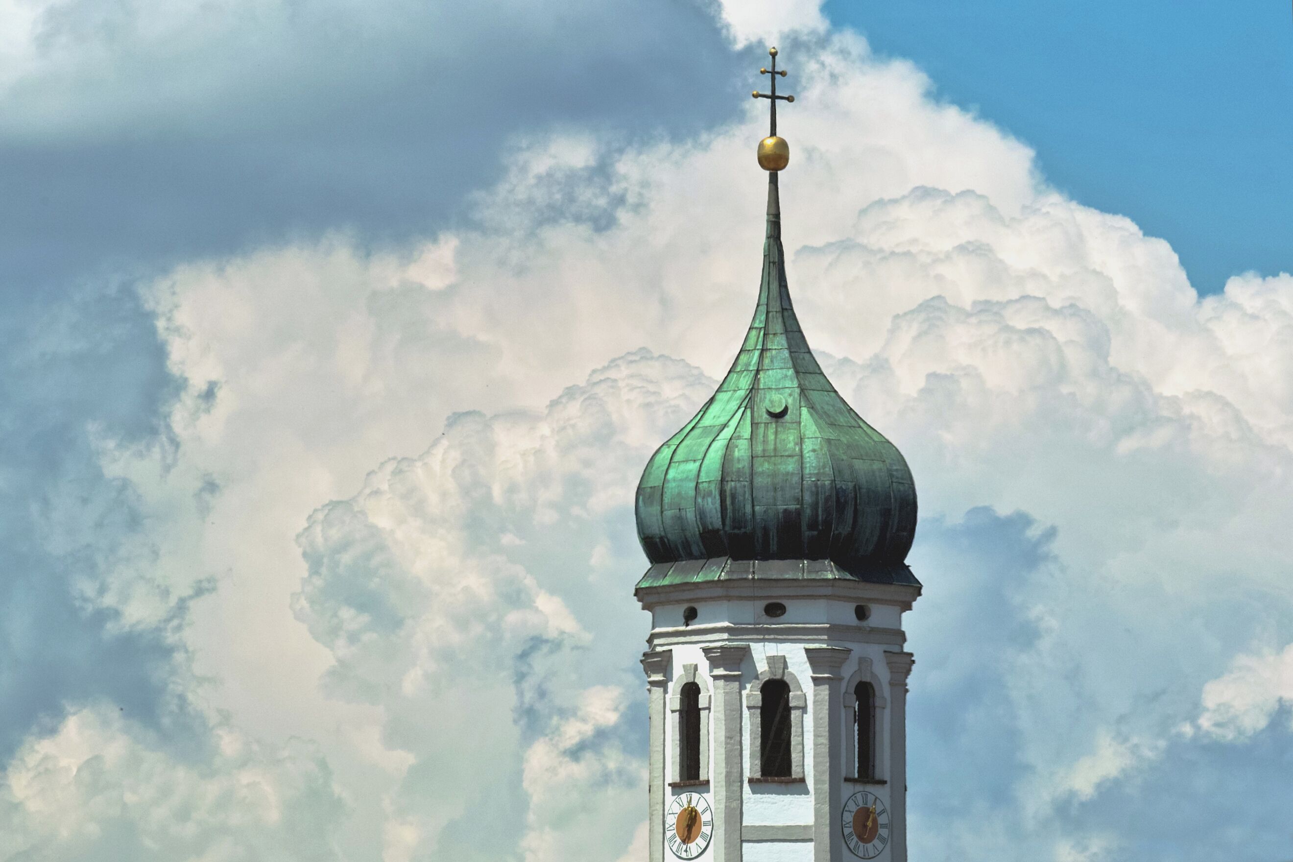 A church tower with a green dome and a golden weather vane.