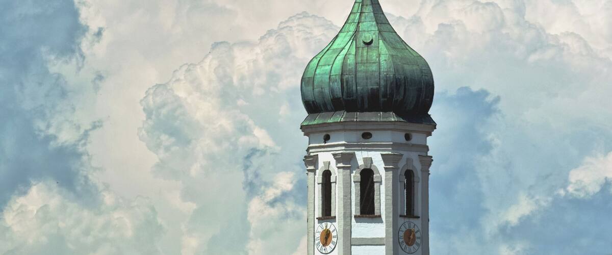 A church tower with a green dome and a golden weather vane.