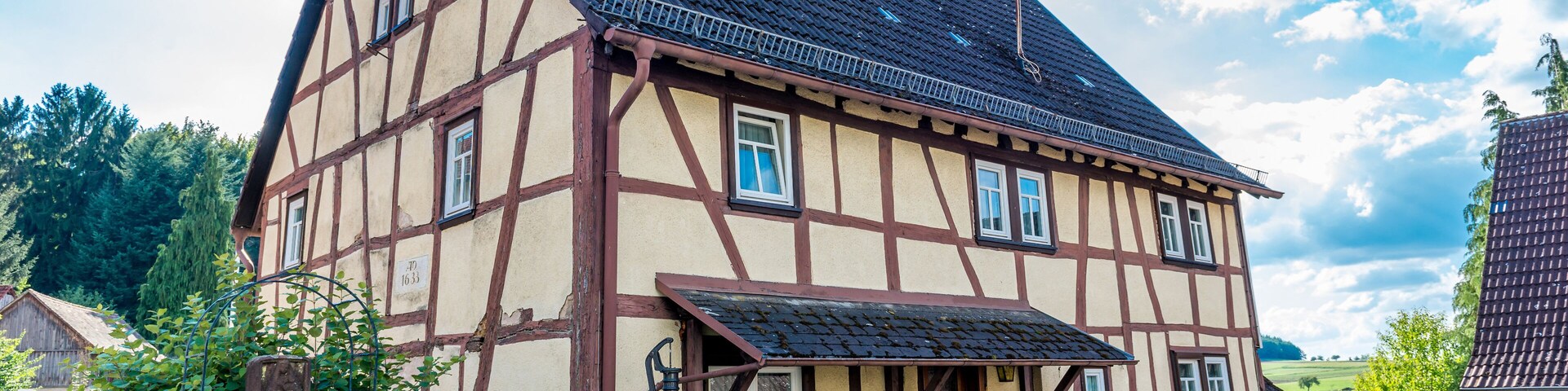 A traditional half-timbered house with a steeply pitched roof, a stone bench, and a wrought iron gate.