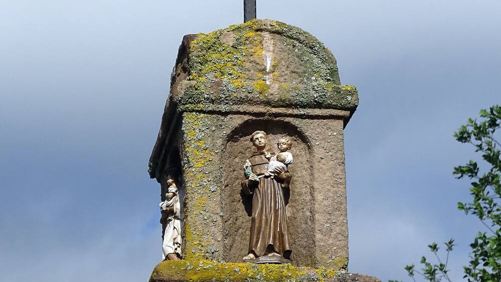 A stone monument with a cross on top, featuring a relief sculpture of a woman holding a child.