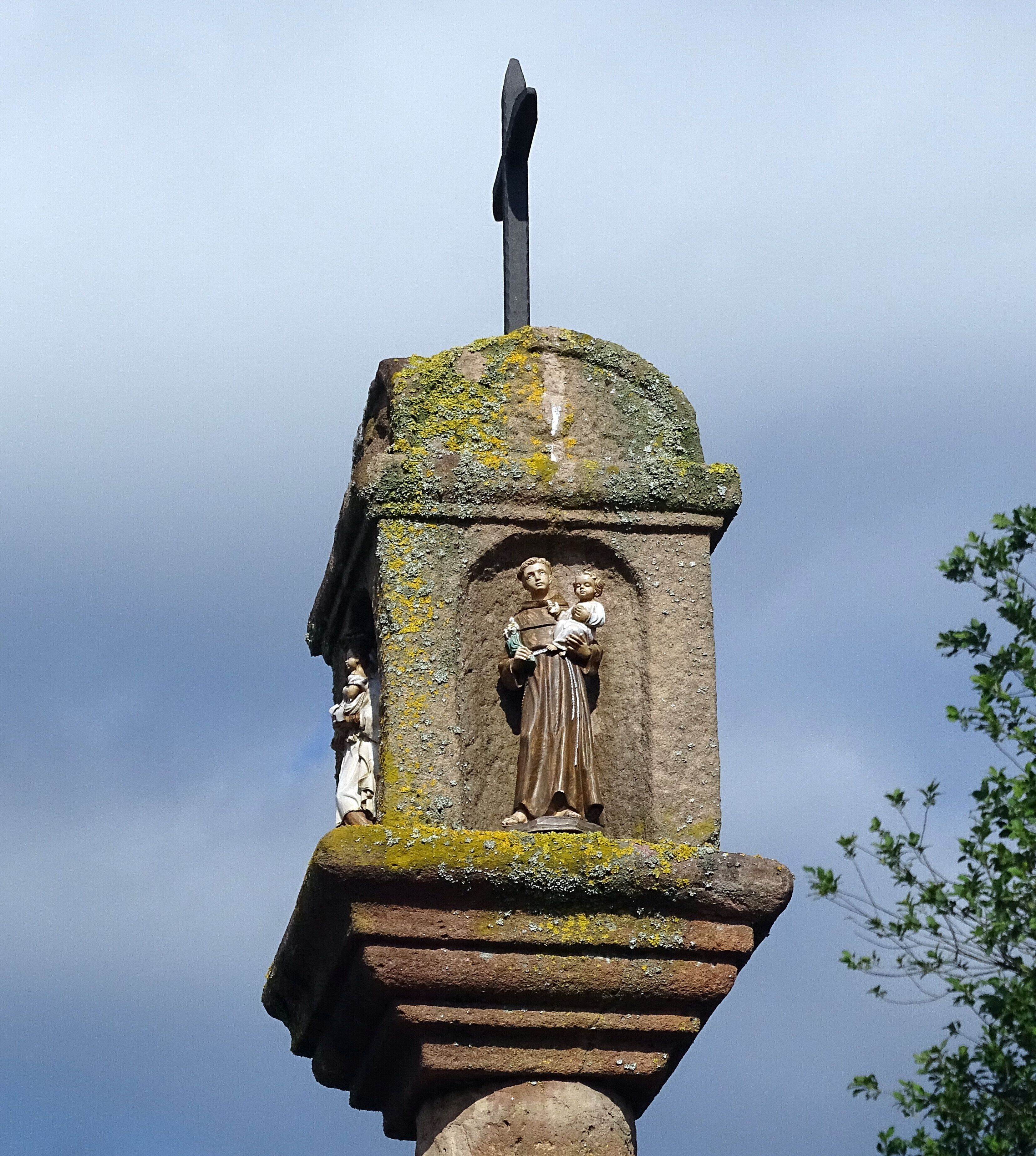 A stone monument with a cross on top, featuring a relief sculpture of a woman holding a child.