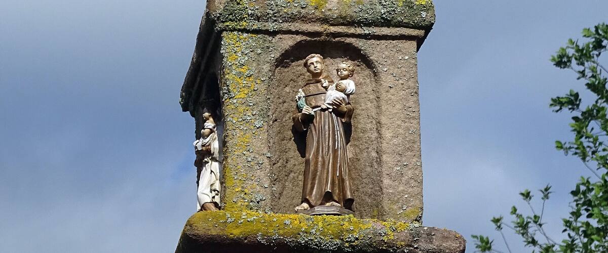 A stone monument with a cross on top, featuring a relief sculpture of a woman holding a child.