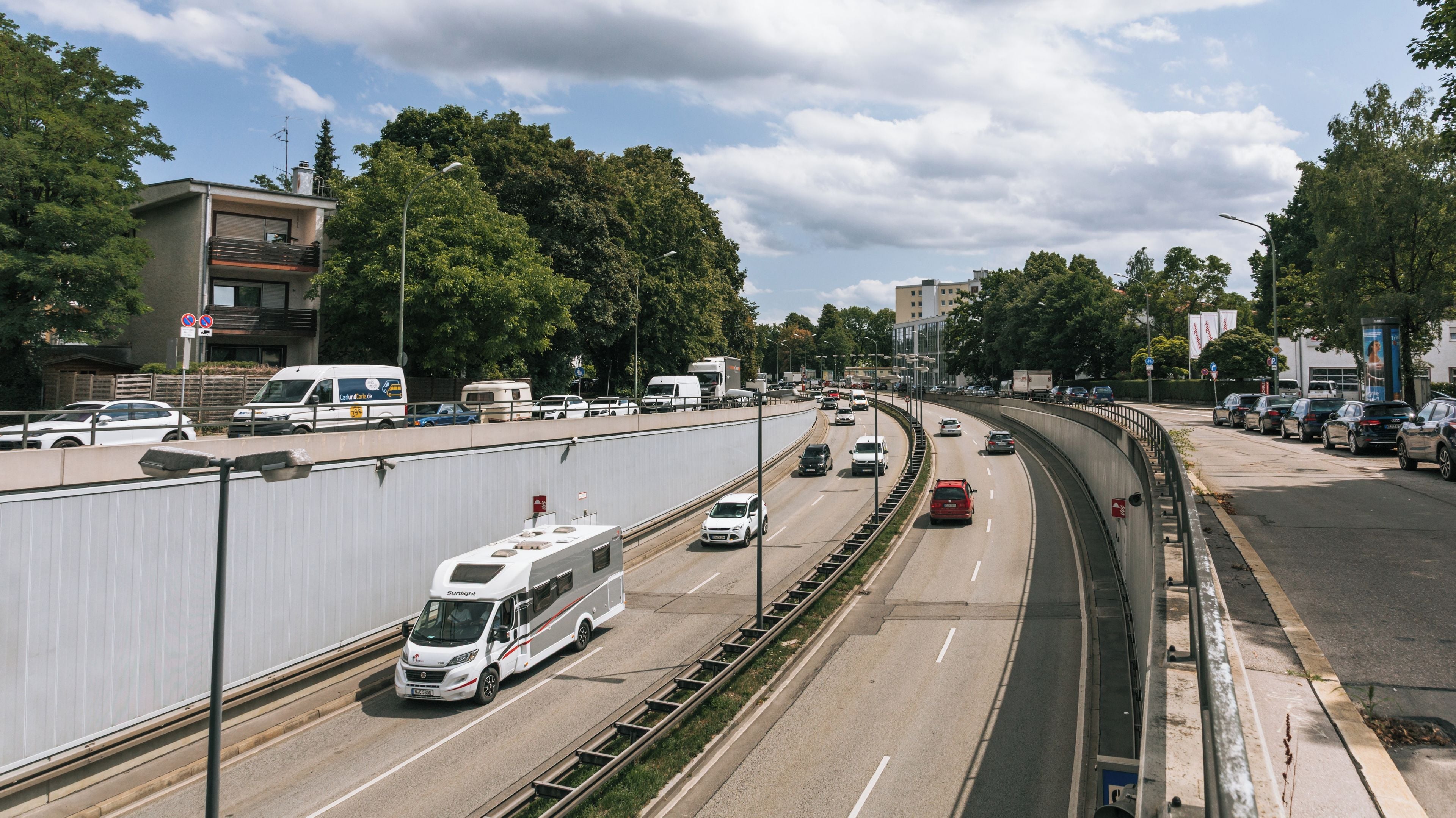 Un'autostrada a più corsie con veicoli, tra cui un camper, sotto un cielo sereno con nuvole.