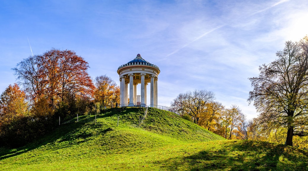 A park with a prominent white columned structure on a hill, surrounded by autumn-colored trees.