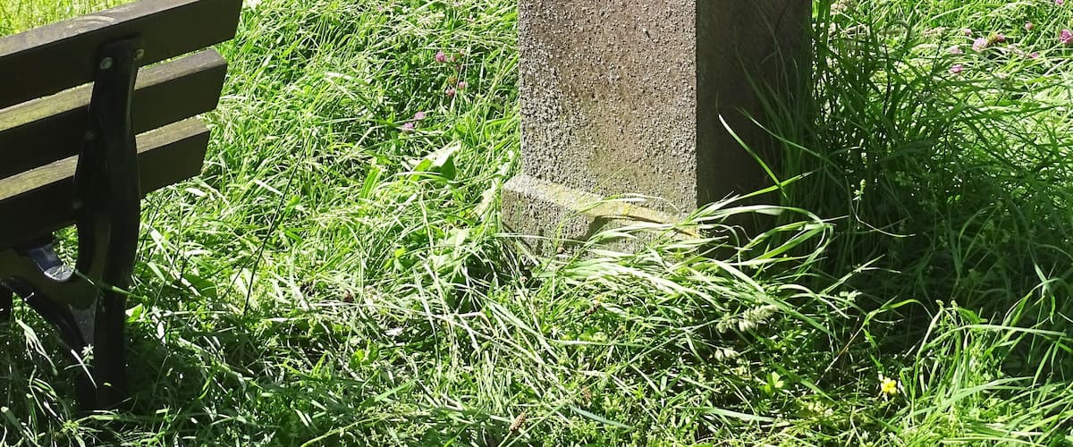 A stone monument with inscriptions, a bench, and a road in a grassy area.