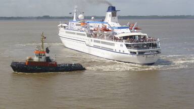 A large cruise ship named 'BERLIN VALLETTA' with a tugboat escorting it.