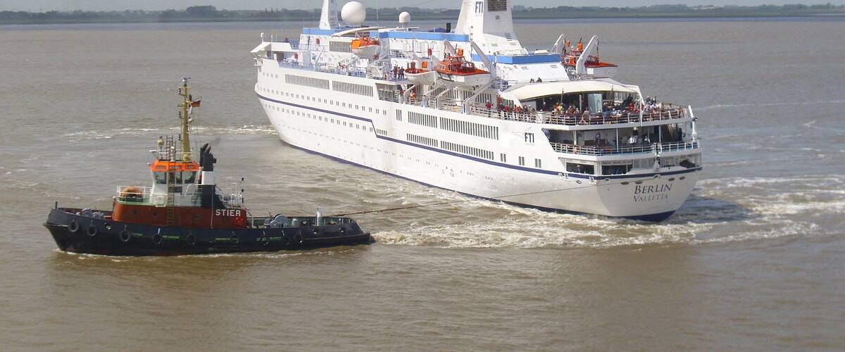 A large cruise ship named 'BERLIN VALLETTA' with a tugboat escorting it.