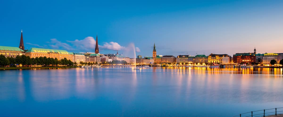Ein ruhiger Fluss mit Stadtansicht im Hintergrund, darunter ein markantes Gebäude mit Gründach und einem hohen Turm.