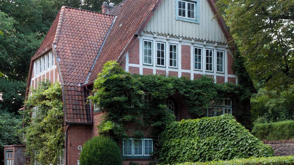 A traditional house with a red-tiled roof, white trim, and a brick facade.