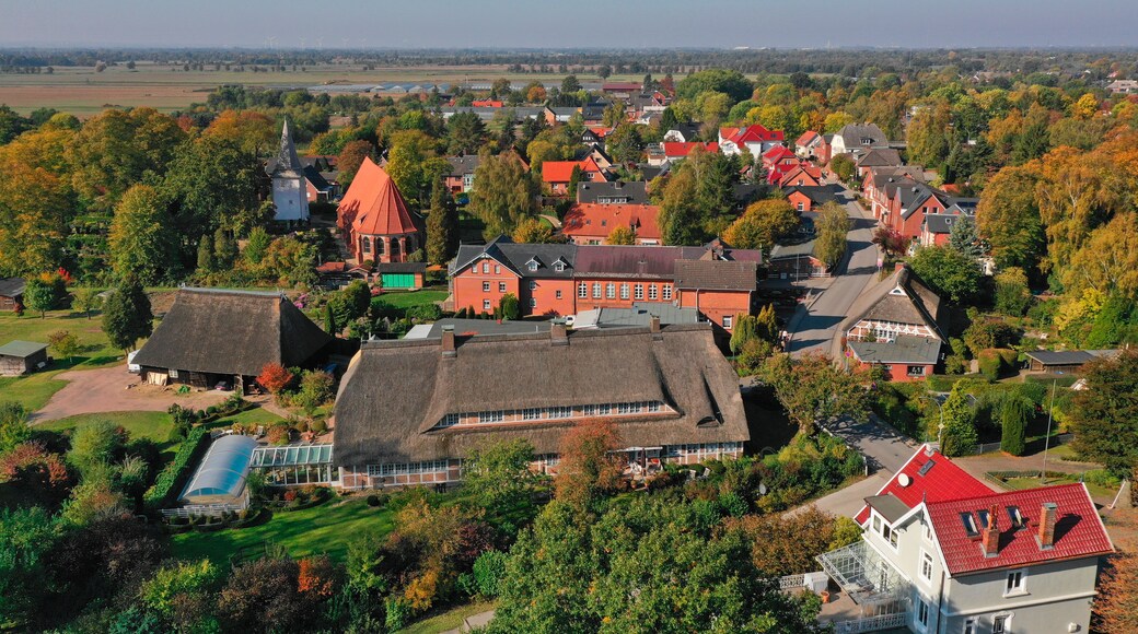 A village with traditional houses, a church, and wind turbines in the distance.