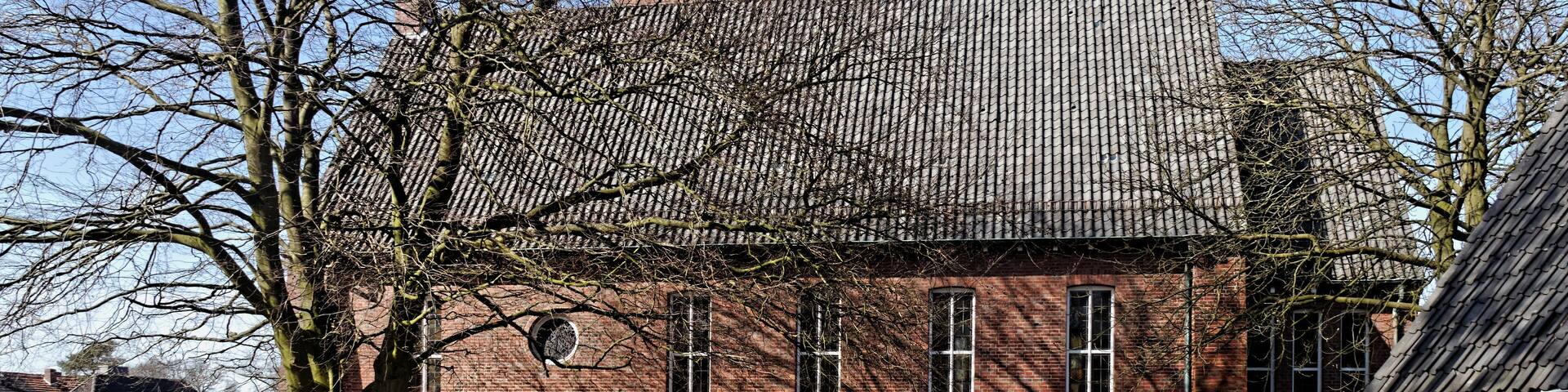 A brick building with a tiled roof, a bell tower, and a large tree in the foreground.