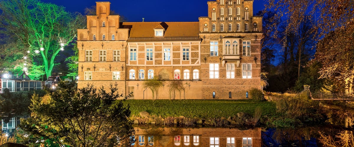 Ein großes, beleuchtetes historisches Gebäude mit einem spiegelnden Teich davor.