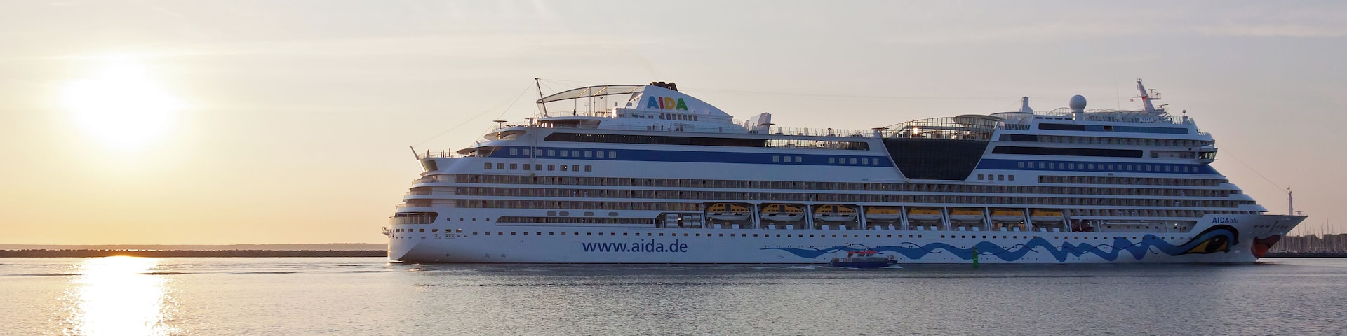 The AIDAblu sailing through the port entrance of Warnemรผnde on the 04th of Juli 2010. The marina of Hohe Dรผne is discernible in the right background of the photograph.