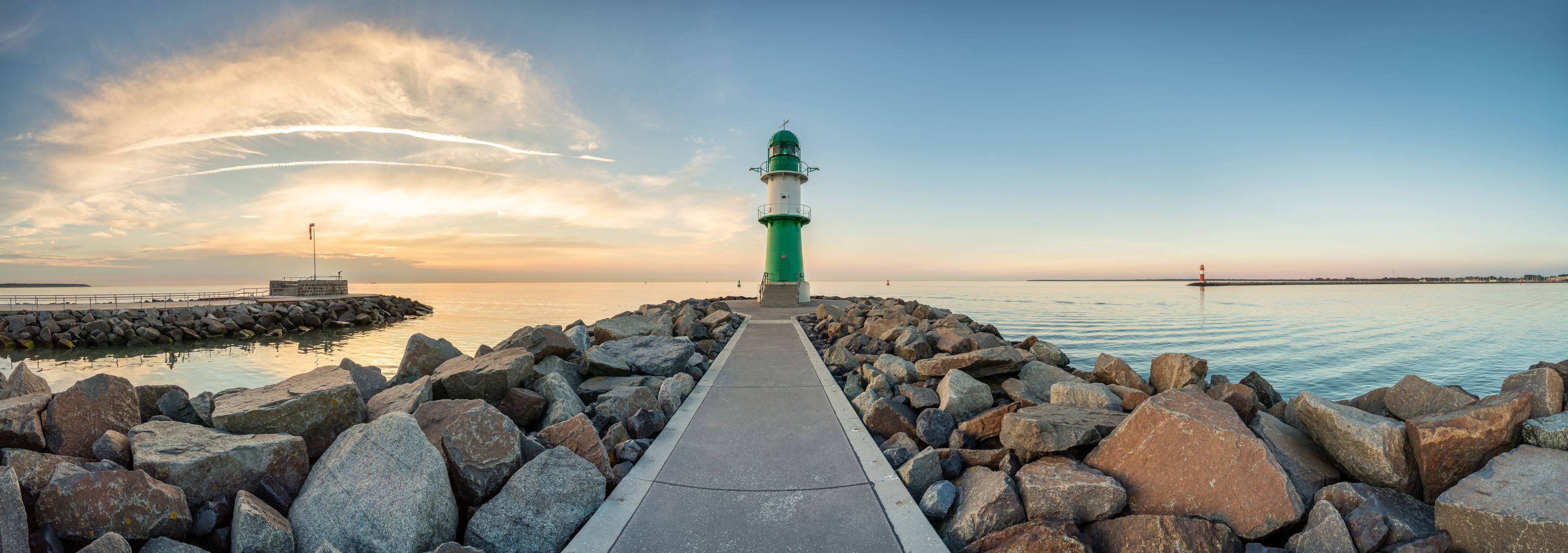 A lighthouse on a rocky pier with a clear sky and calm water.