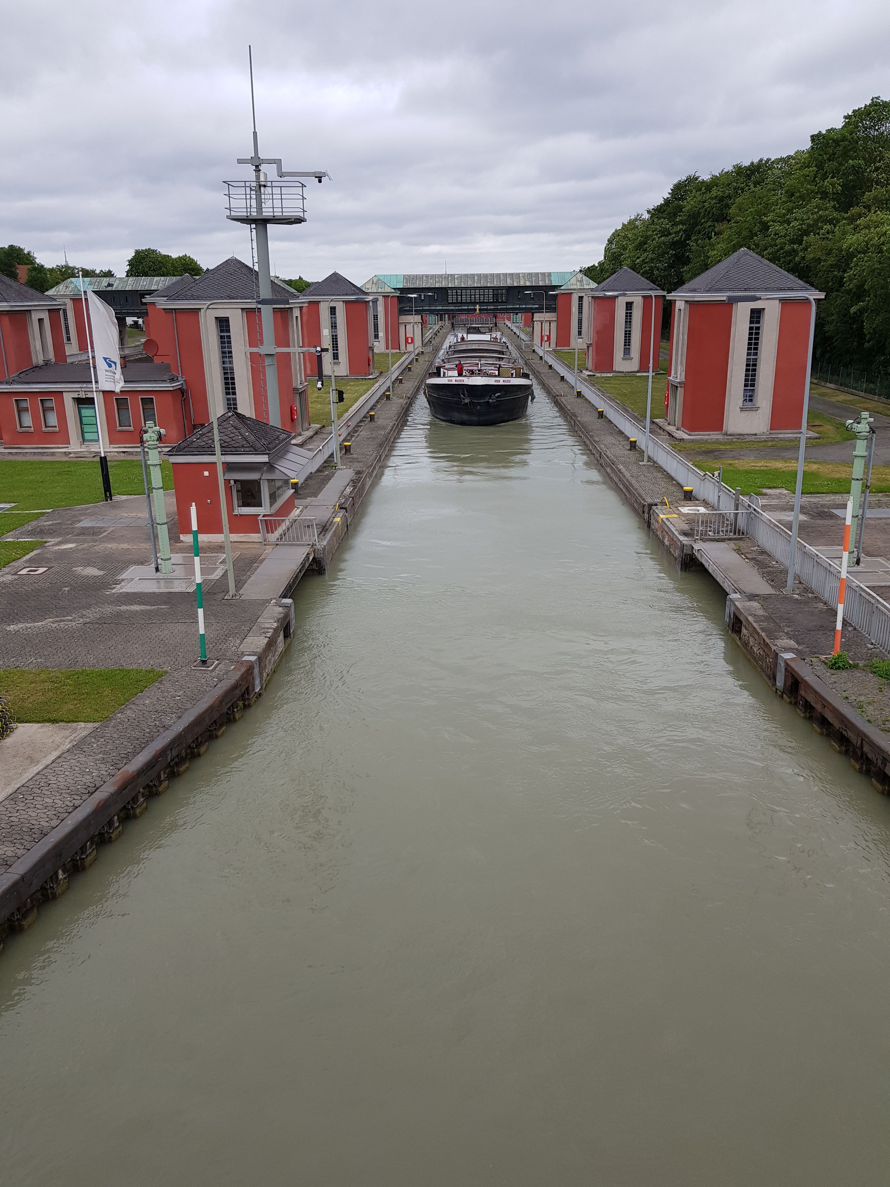 A canal with a boat passing through a lock, surrounded by red buildings and a bridge in the background.