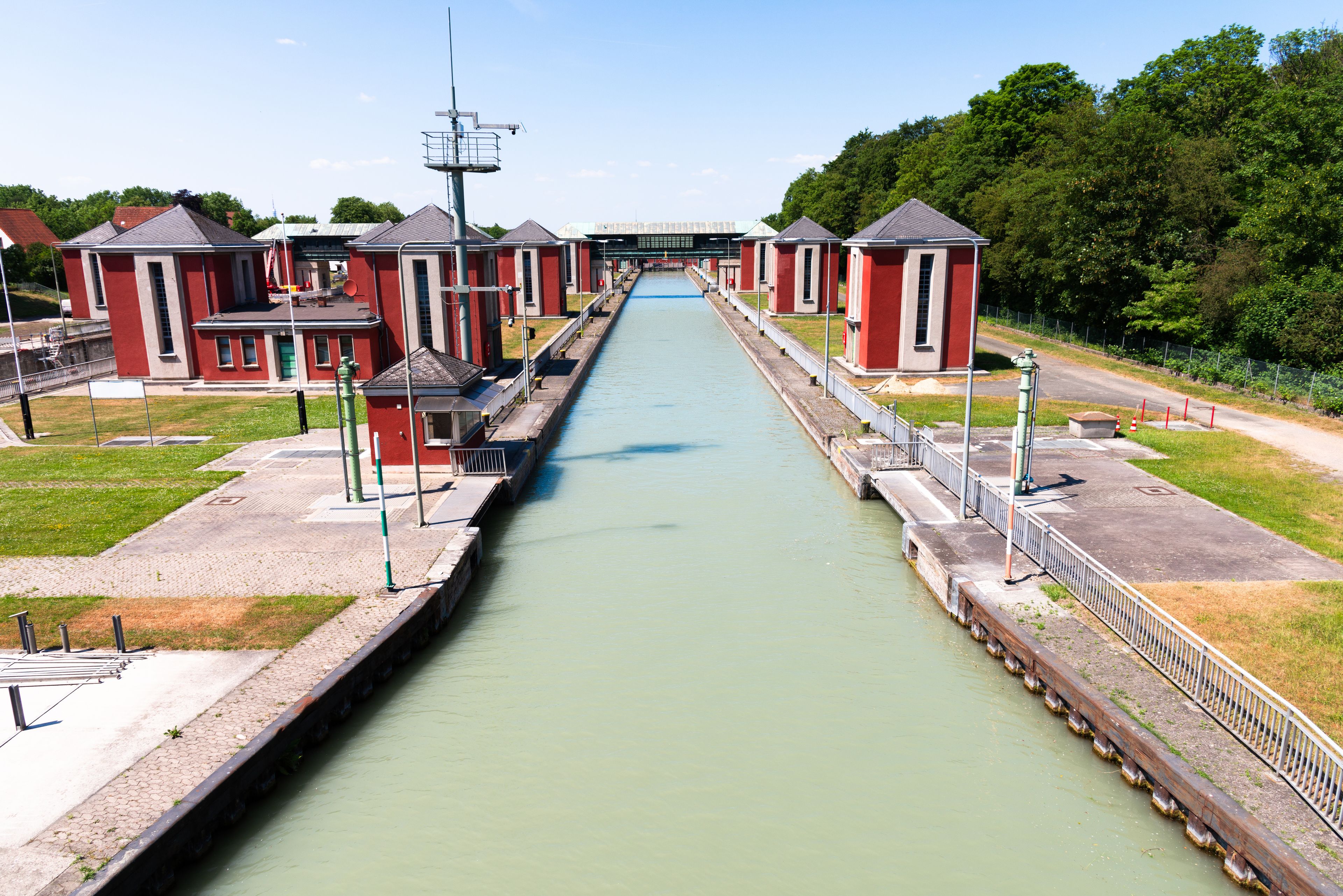 A canal with red buildings on either side, a bridge in the background, and green trees surrounding the area.