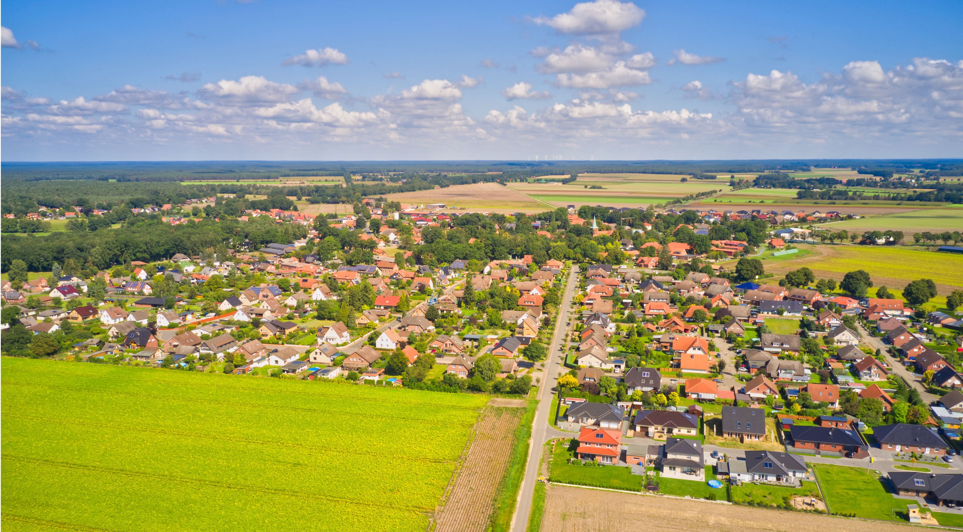 Ländliche Landschaft mit einem Dorf, grünen Feldern und wolkenlosem Himmel.