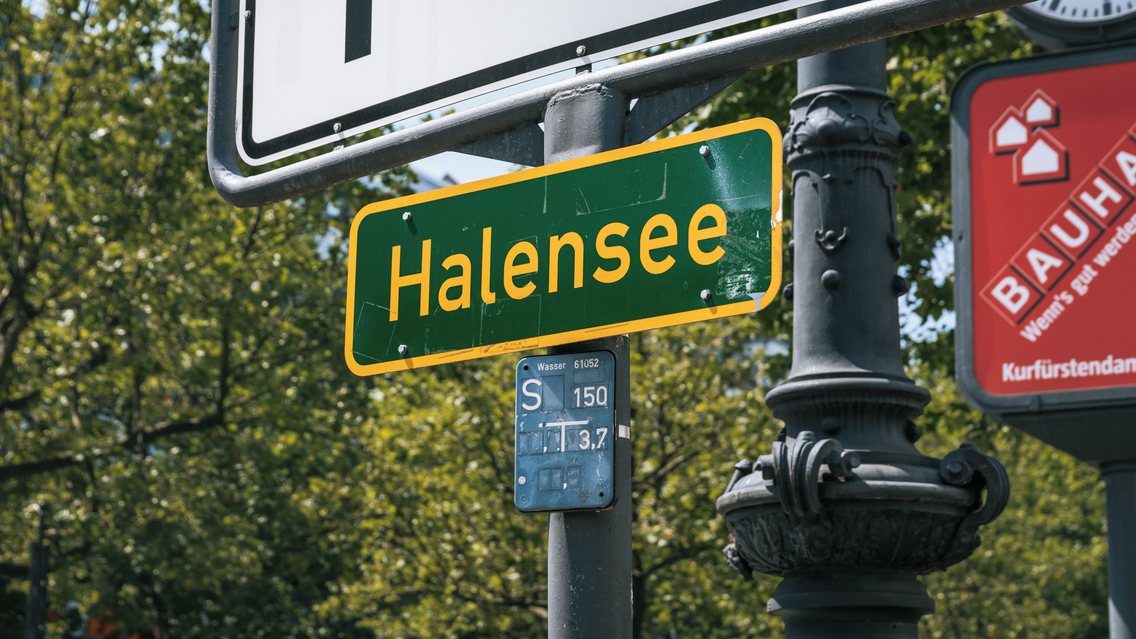 Una señal de calle que indica 'Halensee', con un cartel de estacionamiento debajo y una señal roja con texto blanco parcialmente visible.