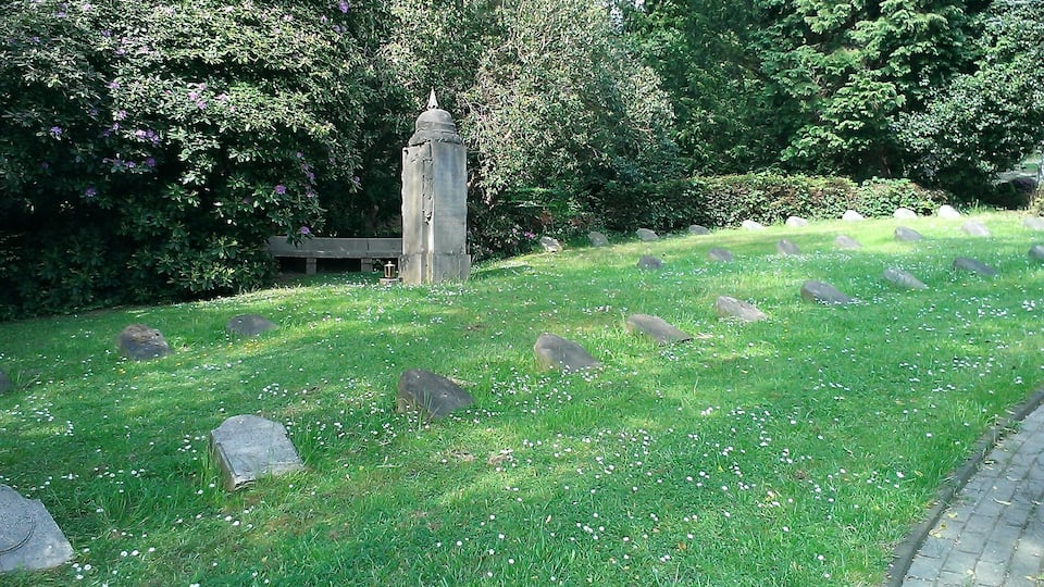 A cemetery with headstones and a central monument surrounded by lush greenery.