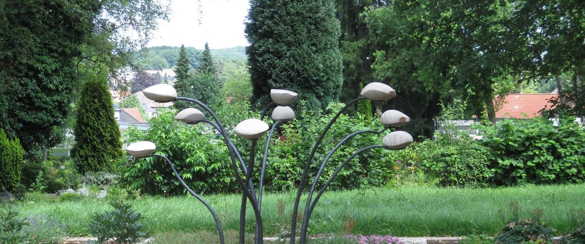 A garden with a stone wall, flowering plants, and a metal sculpture of tree-like structures.
