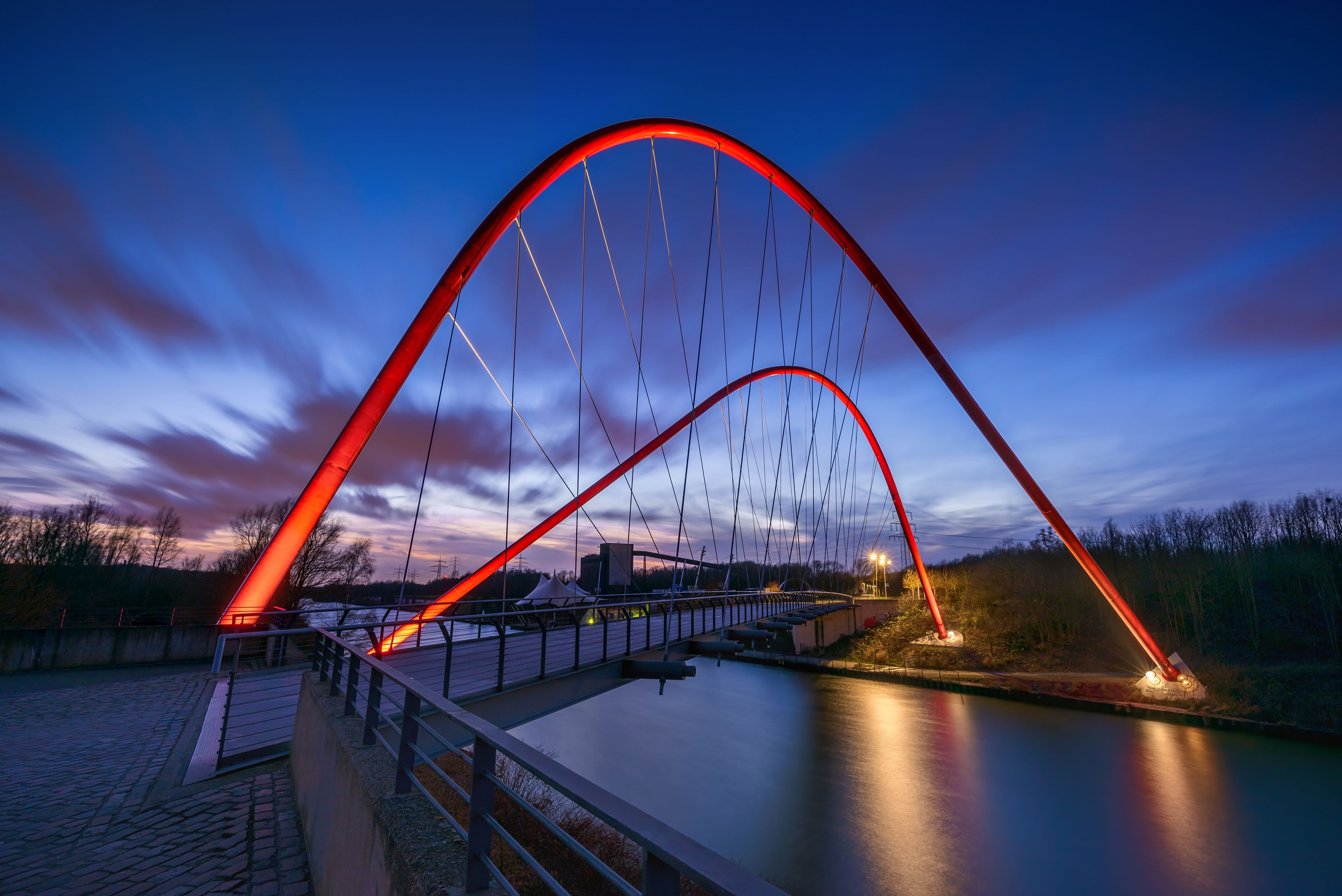 Un puente rojo en arco sobre un río tranquilo al anochecer.