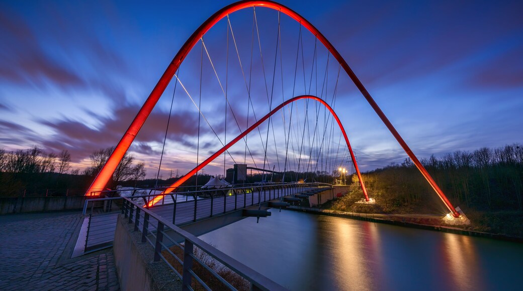 Un puente rojo en arco sobre un río tranquilo al anochecer.