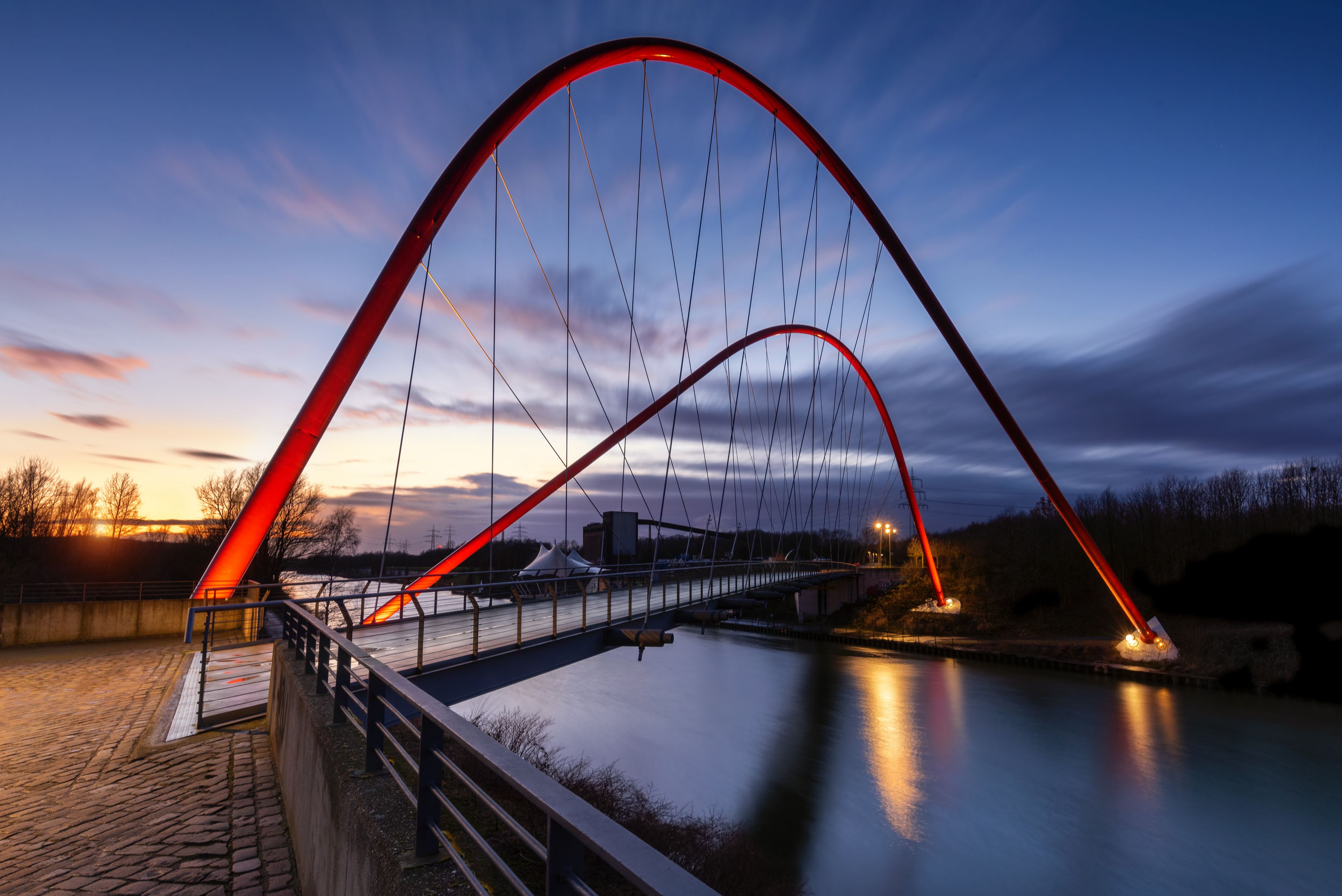 Un puente con arcos rojos sobre un río al anochecer.