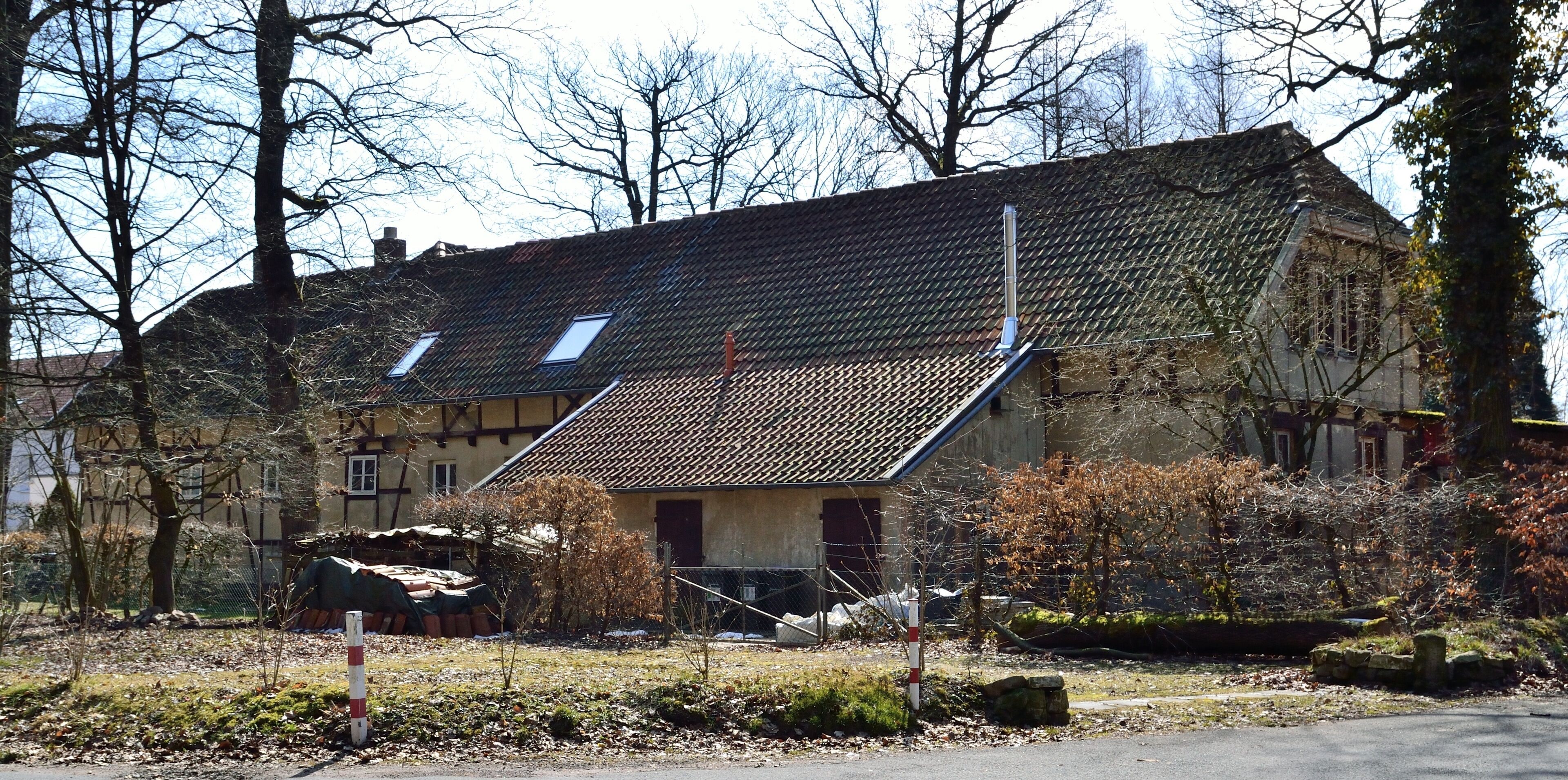 A traditional house with a sloped roof, surrounded by trees and a stone wall.