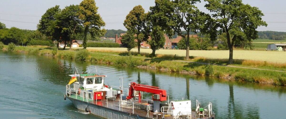 A boat named 'Teuto' on a calm river surrounded by greenery and houses.