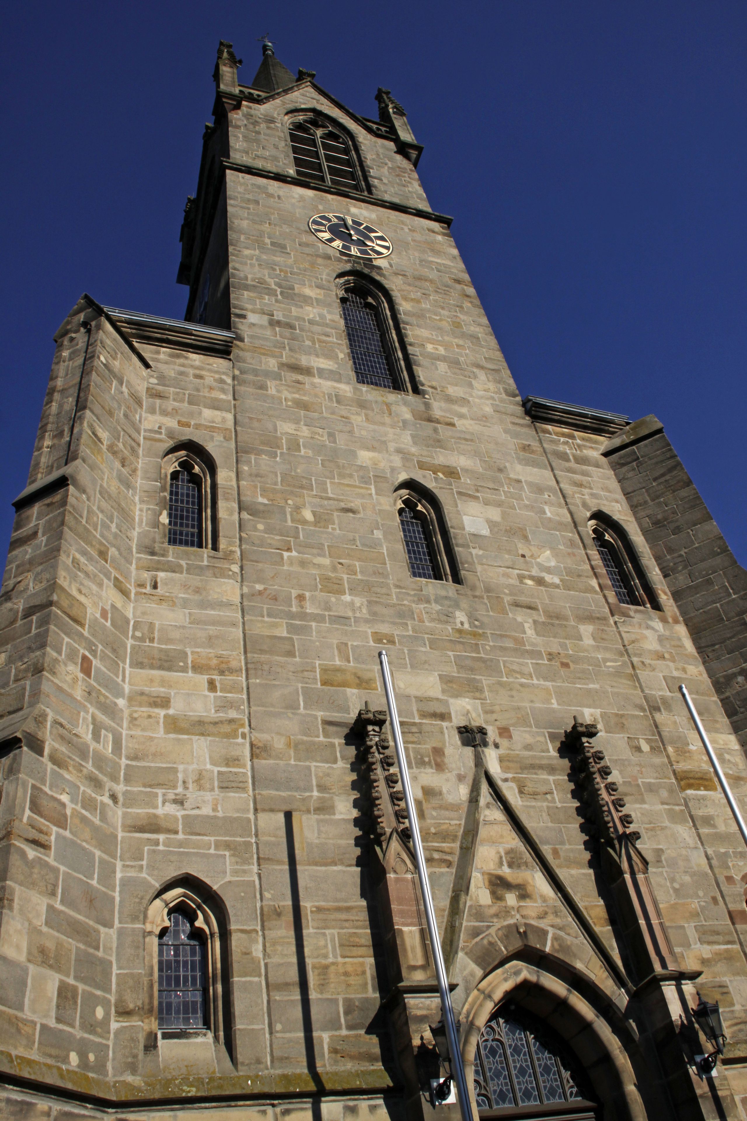 A tall stone tower with a clock, arched windows, and a pointed roof.