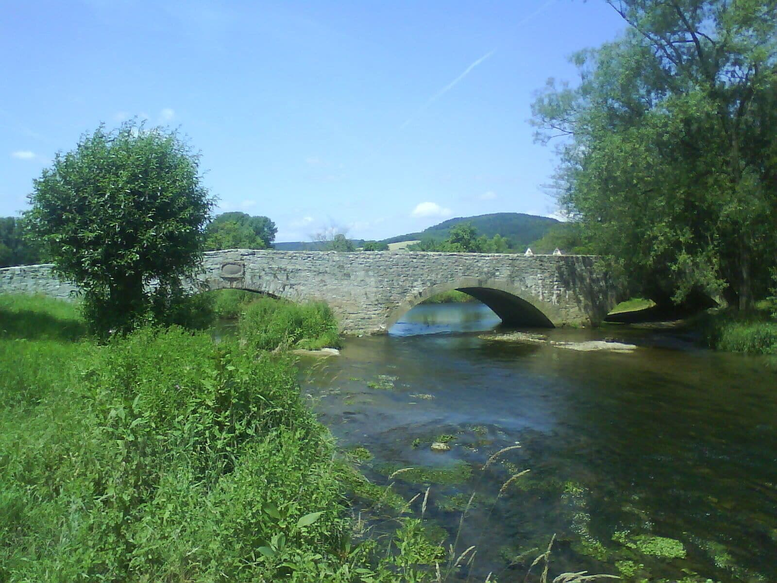 A stone bridge over a river with greenery on both sides.