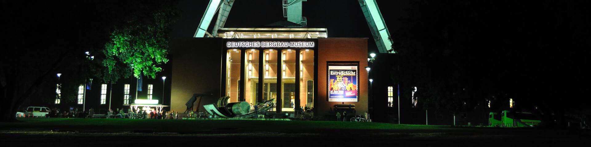 A lit structure resembling a crane at night, with a building labeled 'DEUTSCHES BERGBAU-MUSEUM' in front.