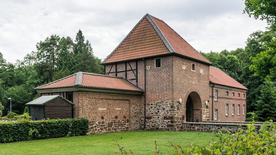 A historic brick building with a red-tiled roof and a stone archway.