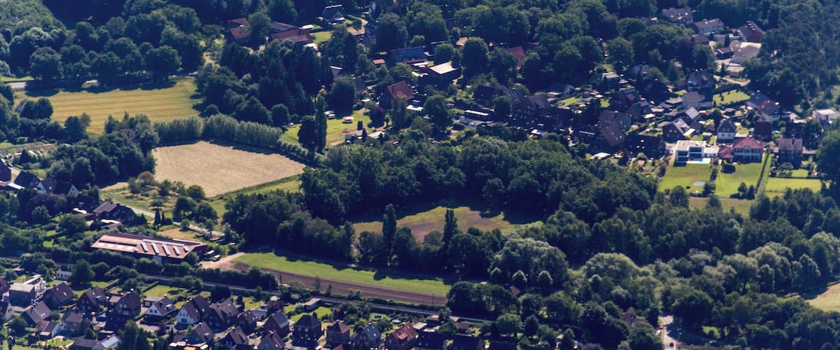 An aerial view of a rural village with houses, fields, and dense forests.