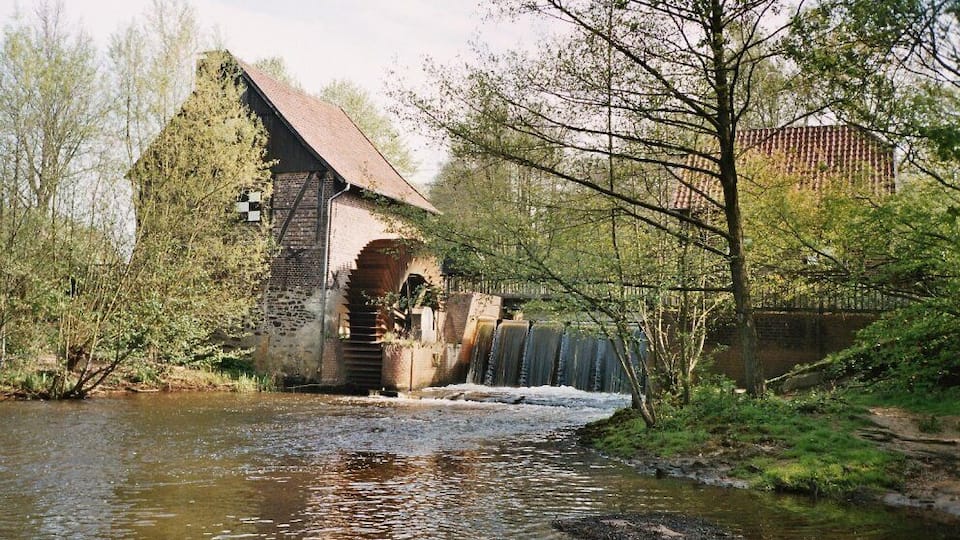 A watermill by a river with a stone building and a weir.