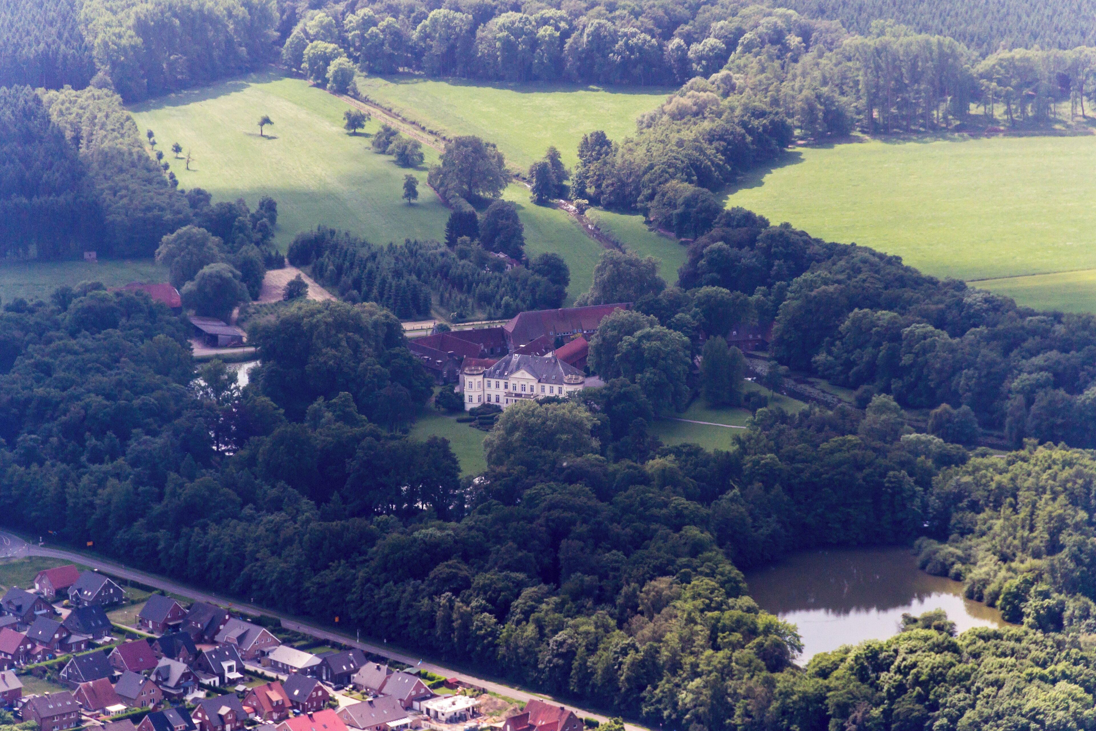 An aerial view of a large estate with a prominent manor house surrounded by lush greenery and a lake.