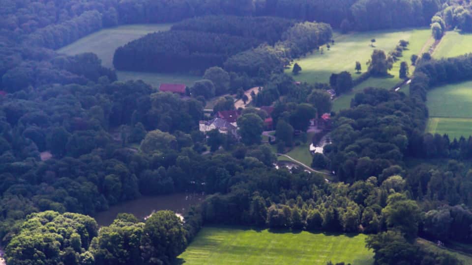 A lush green landscape with rolling hills, dense forests, and scattered houses.